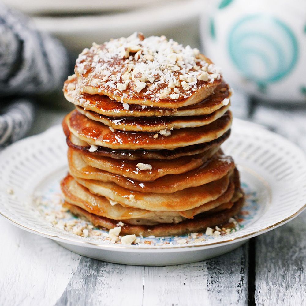 Stapel pannenkoeken met bruine vloeistof en noten. Op een bord.