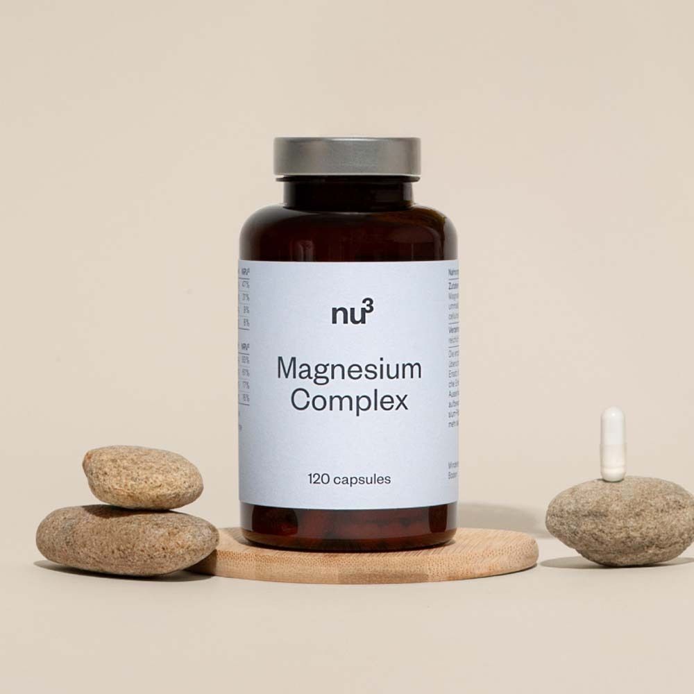 Bruine fles met wit etiket, opschrift « Magnesium Complex » en « 120 capsules ». Op houten plank met stenen.