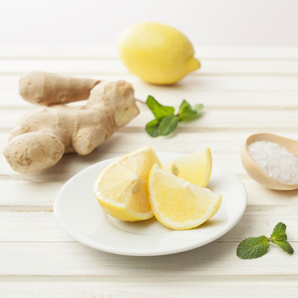 Citroenschijfjes op een bord, daarnaast gember, munt en zout. Op een lichte houten ondergrond.