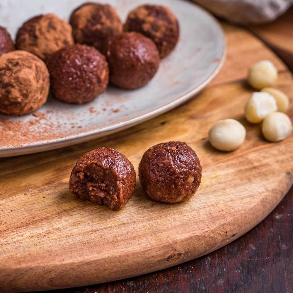 Cacaoballen op houten plank. Sommige ballen zijn doorgesneden, met macadamia-noten.