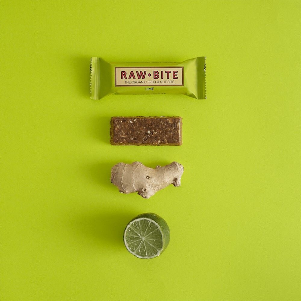 Reep, gember en limoen op groene achtergrond. Opschrift: "RAW BITE", "THE ORGANIC FRUIT & NUT BITE" en "LIME".