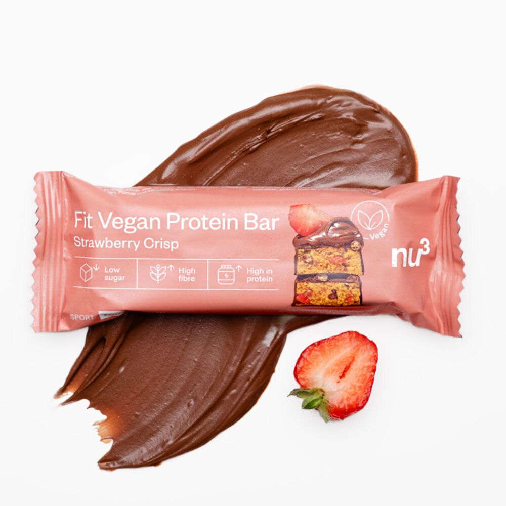 Barre protéinée dans un emballage rose, à côté de crème au chocolat et de fraise. Nom et logo du produit visibles.