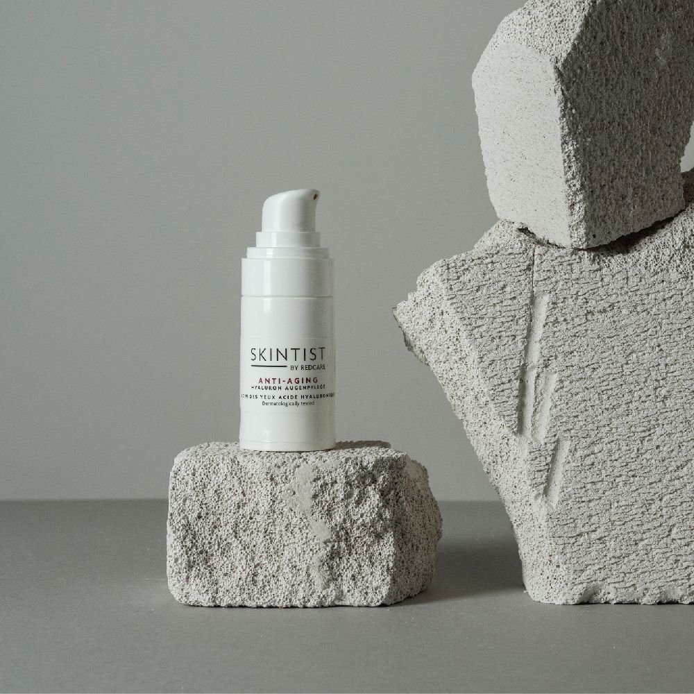 Witte fles met pomp op een steen. Opschrift: SKINTIST BY REDCARE ANTI-AGING Hyaluron Augenpflege.