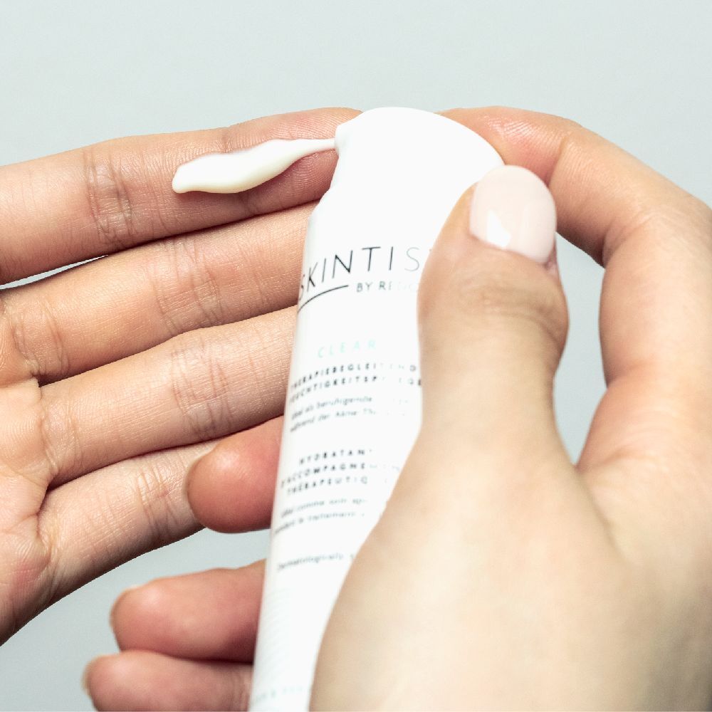 Handen houden een tube SKINTIST CLEAR vast. Crème wordt uit de tube geperst.