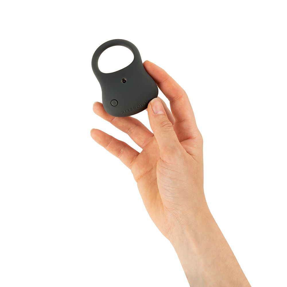Grijze penisring met knoppen, vastgehouden in een hand. Ringvormige opening zichtbaar.