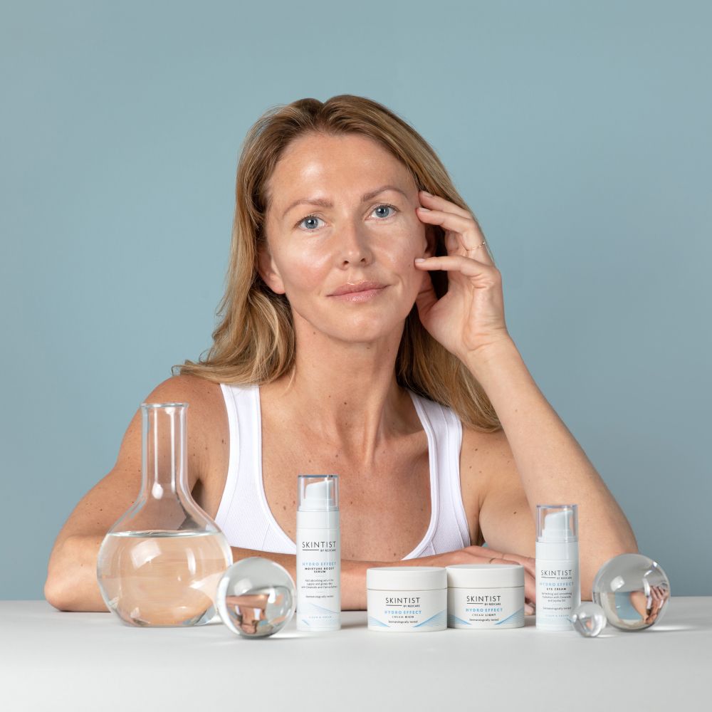 Vrouw zit voor producten. Zichtbaar: flessen, potten, glazen bollen.