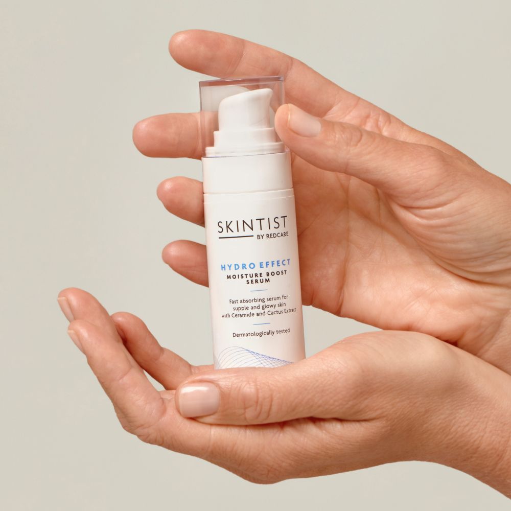 Un flacon blanc avec pompe dans les mains. Inscription: SKINTIST HYDRO EFFECT MOISTURE BOOST SERUM.