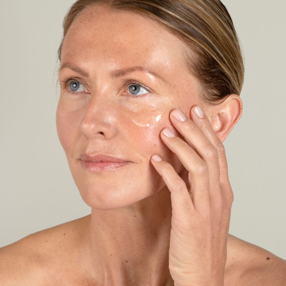 Visage d'une femme avec sérum sur la peau. Aucune désignation de produit visible.
