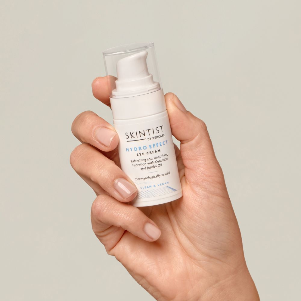 Un flacon blanc de crème pour les yeux SKINTIST HYDRO EFFECT dans une main. Inscription : Rafraîchissant et lissant avec céramide et huile de jojoba.
