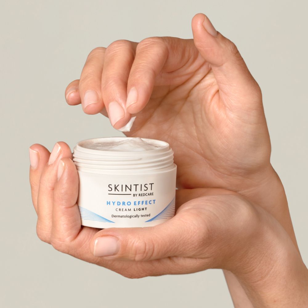 Mains tenant un pot blanc de SKINTIST HYDRO EFFECT Cream Light. Le couvercle est ouvert.