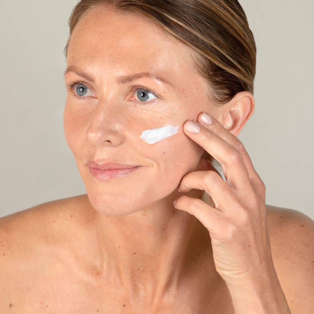 Femme appliquant de la crème sur la joue. La crème est blanche.
