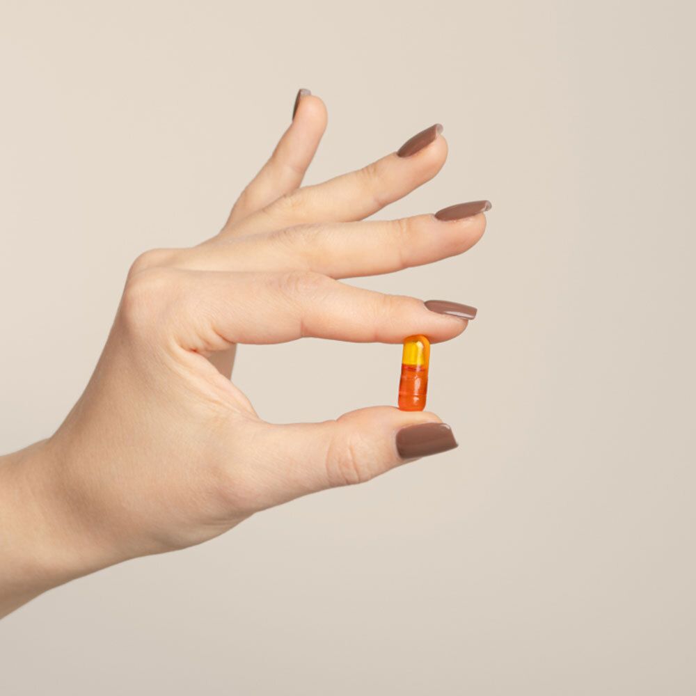 Hand houdt een oranje capsule vast. Bruine nagels.