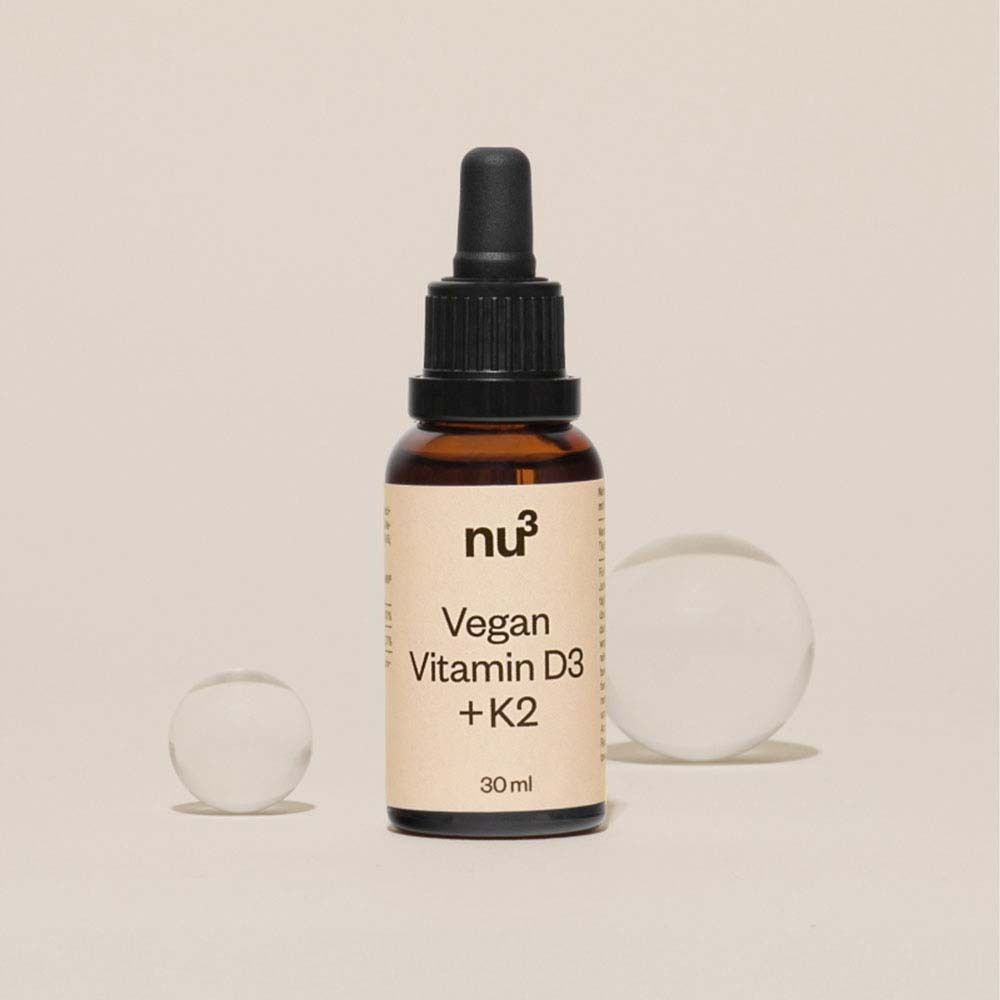 Eén flacon nu3 Vegan Vitamine D3 + K2 (30 ml) op een lichte achtergrond met glazen bollen.
