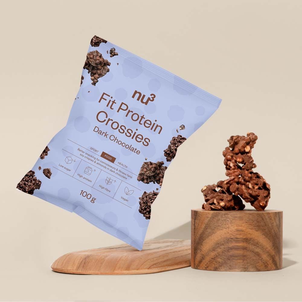 Productverpakking van nu3 Fit Protein Crossies, pure chocolade, op een houten sokkel. Daarnaast een houten plank.