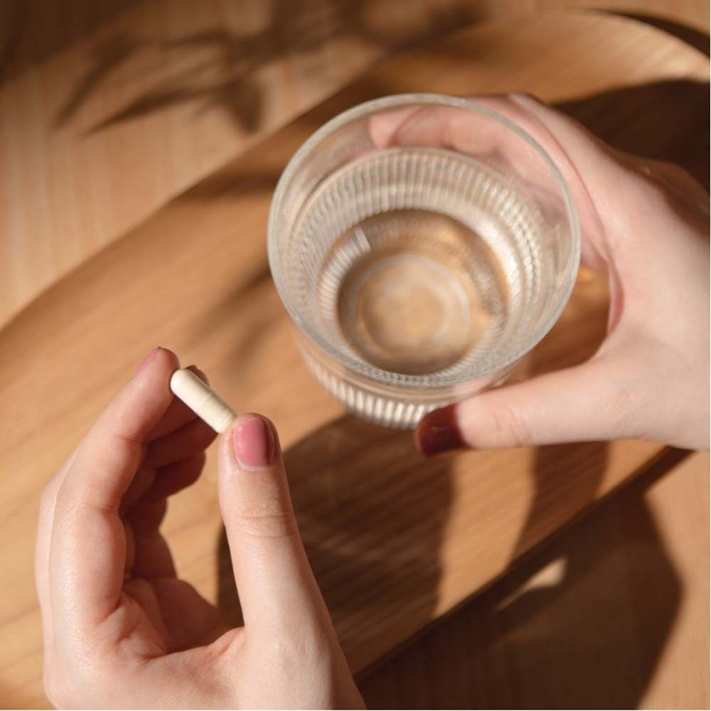 Handen houden een capsule en een glas water. Capsule is licht, water helder.