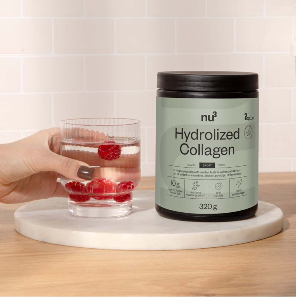 Een pot nu3 Hydrolyzed Collagen naast een glas water met frambozen. Pot met groen etiket, productinformatie en logo. 320g.