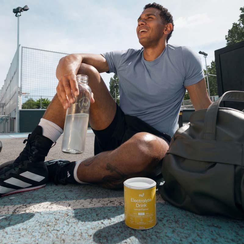 Man zit na het sporten naast Nu3 Elektrolyte Drink blik en waterfles.