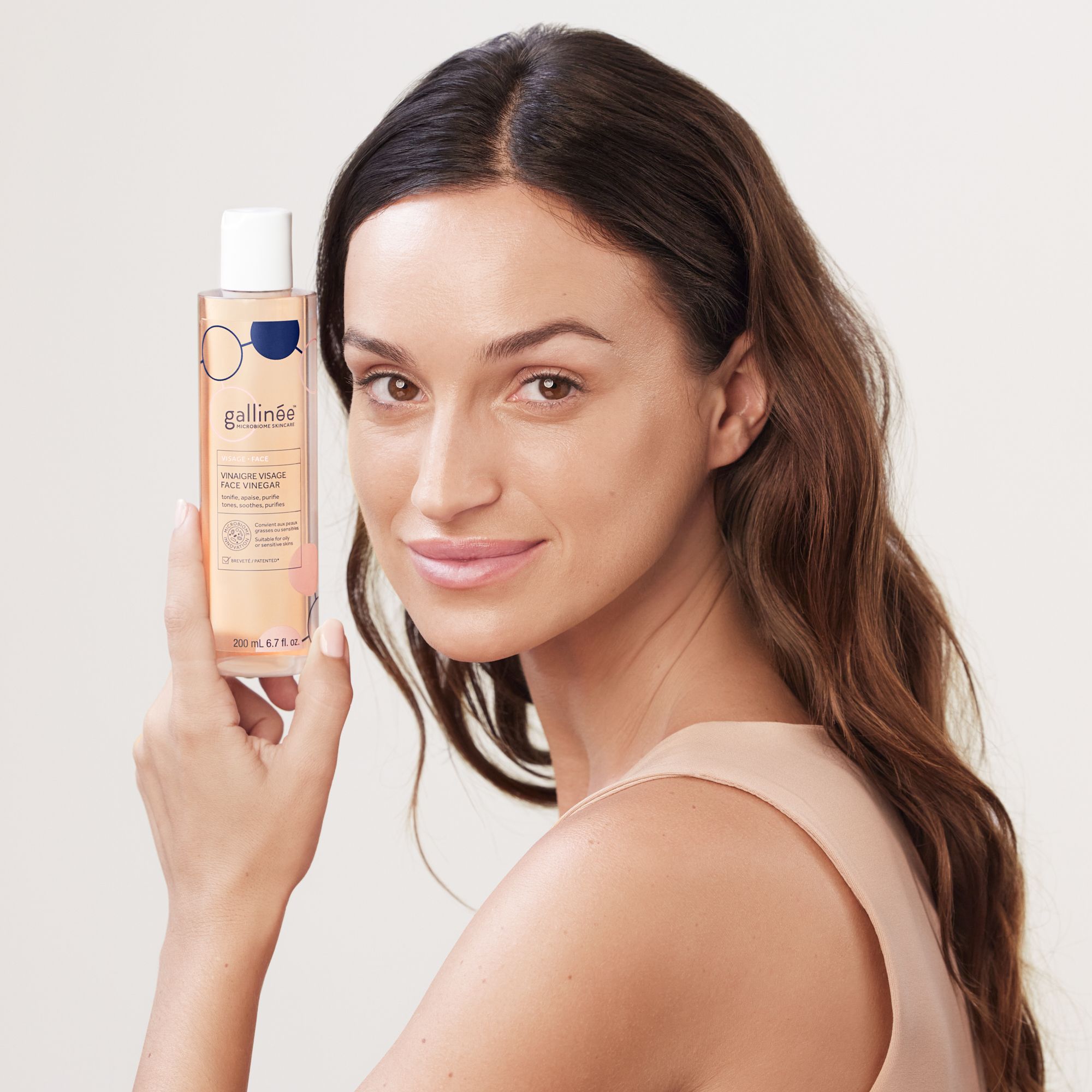Femme tenant un flacon de Face Vinegar. Elle sourit. Flacon avec bouchon blanc et étiquette.