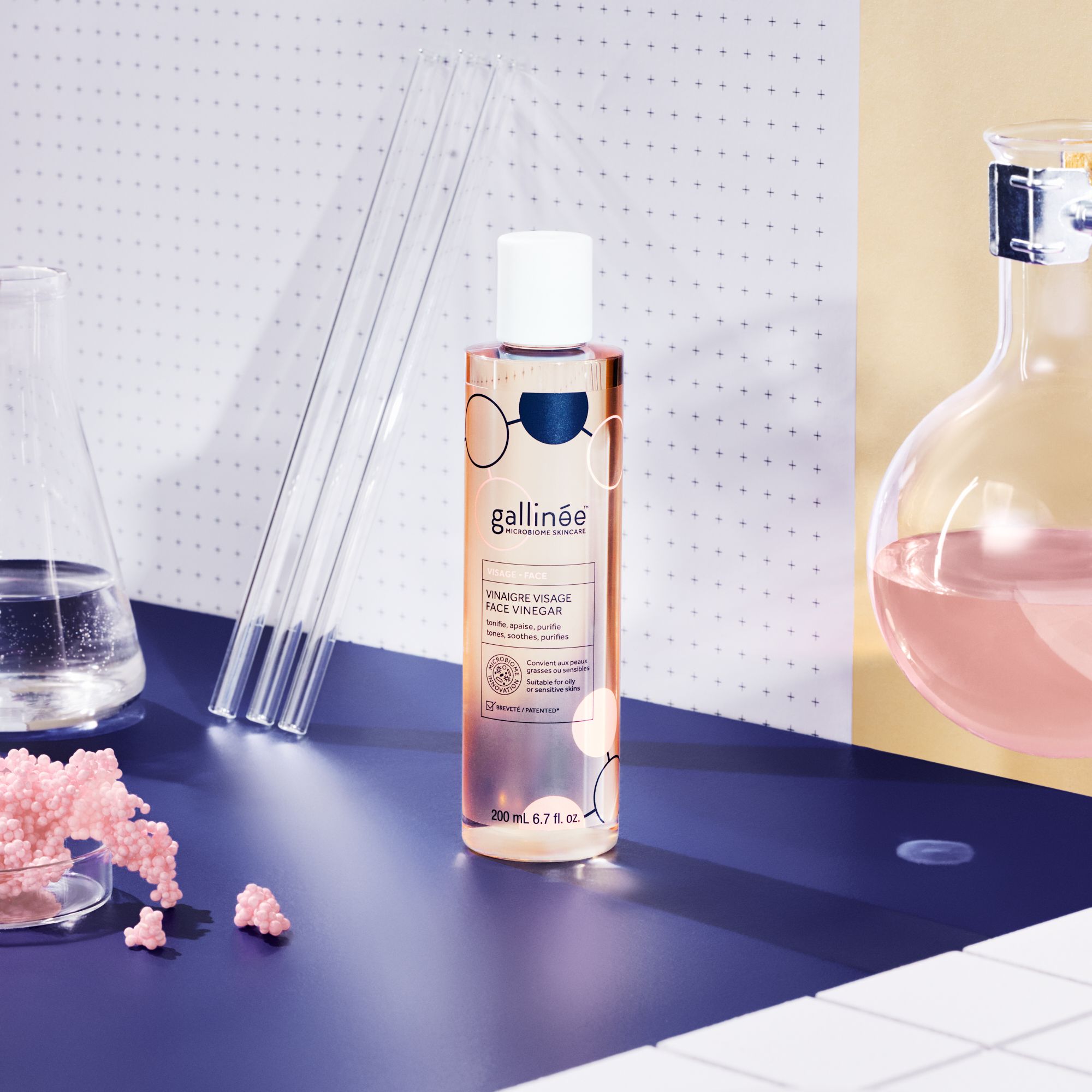 Face Vinegar fles op blauwe tafel. Reageerbuizen, roze decoratie. Achtergrond: wit, blauw, geel.