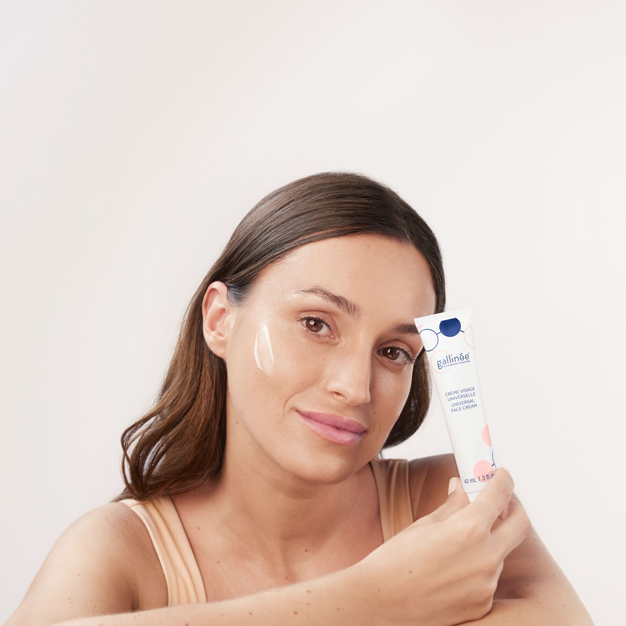 Vrouw met crème op wang. Crèmetube in de hand. Tekst: Crème Visage Universelle.