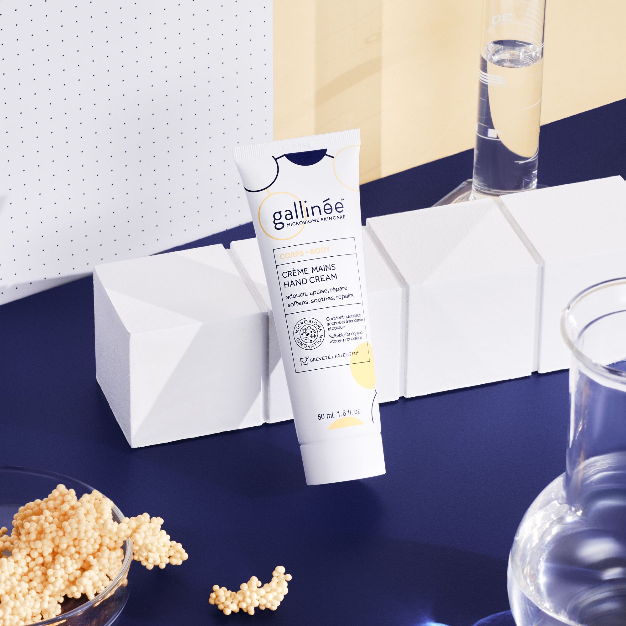 Tube de crème pour les mains Gallinée sur fond bleu. Formes géométriques blanches, récipients en verre et billes.