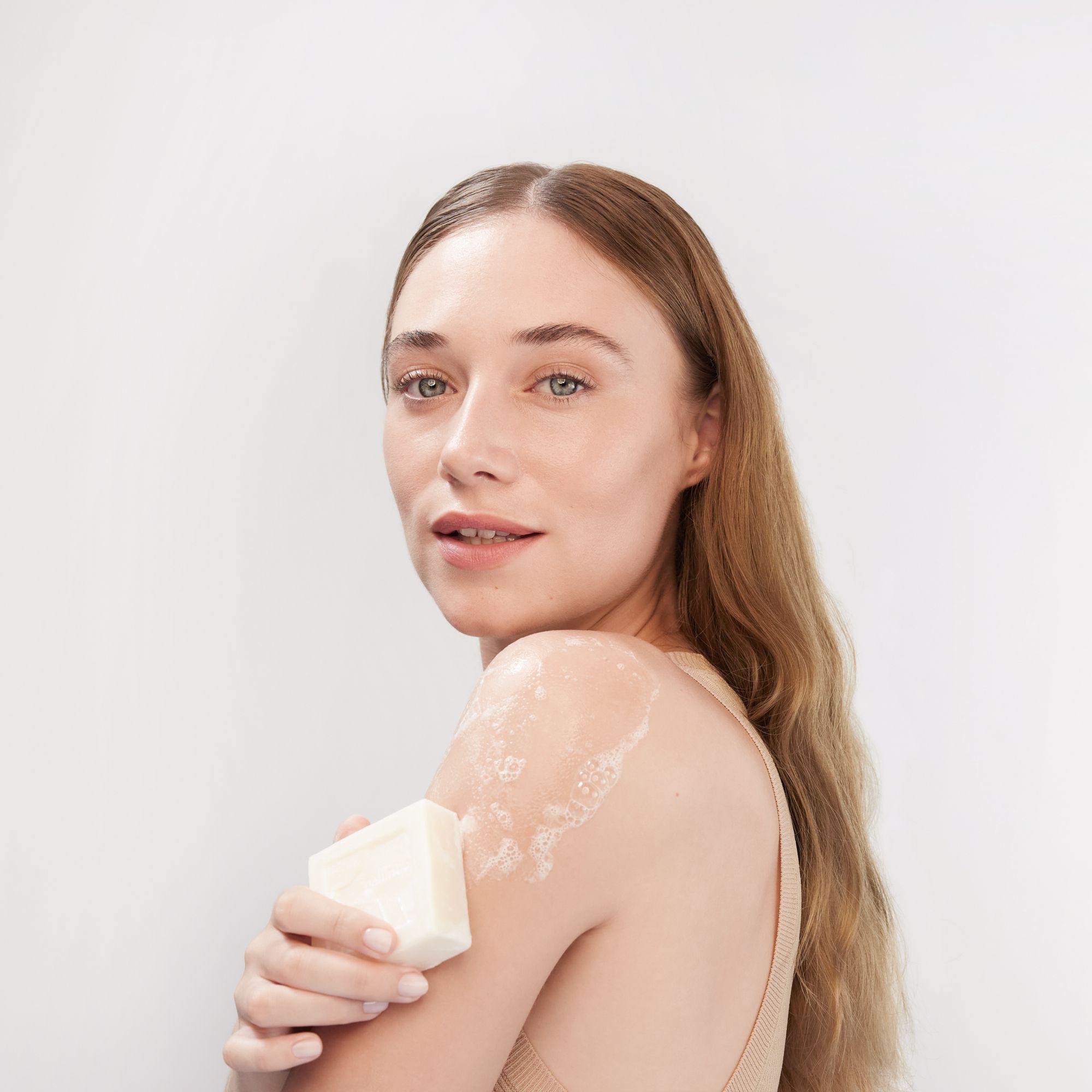 Femme se lavant avec du savon. Le savon est rectangulaire et crème. De la mousse est visible.