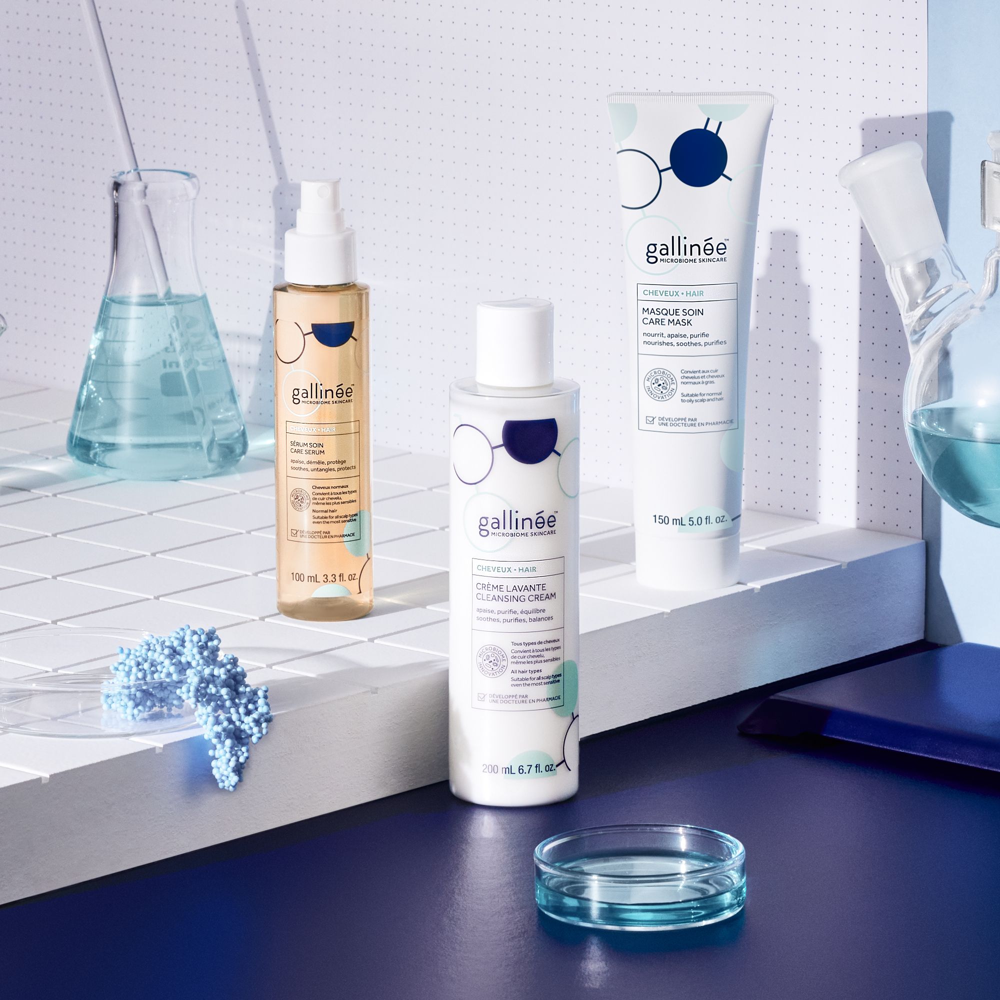 Trois produits Gallinée : sérum capillaire, lotion nettoyante, masque capillaire. Sur fond bleu.
