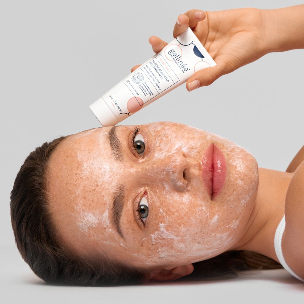 Une main tenant un tube Gallinée au-dessus du visage d'une femme portant un masque.