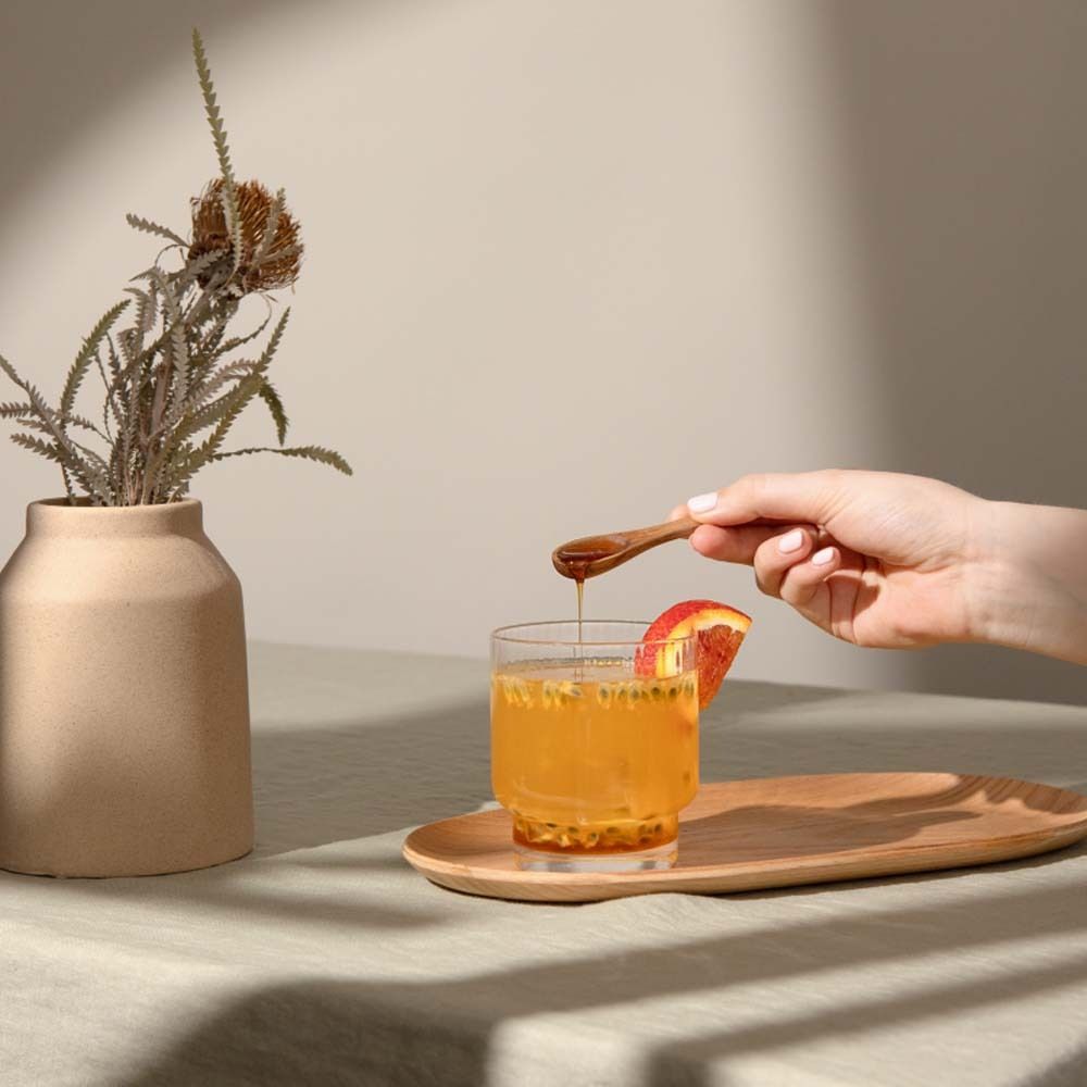 Glas met drank, houten dienblad, hand met lepel, vaas met tak.