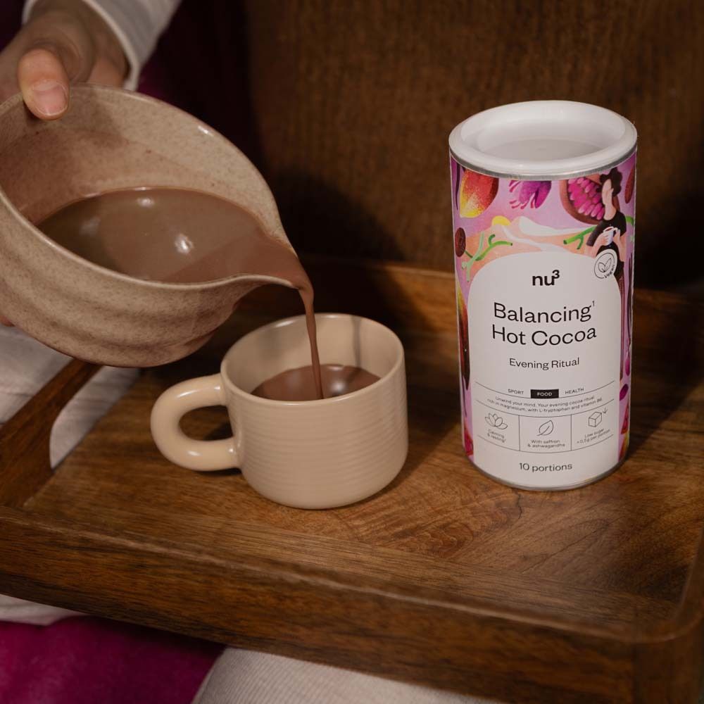 Persoon giet cacao uit een kom in een kopje. Daarnaast staat een doos nu3 Balancing Hot Cocoa.