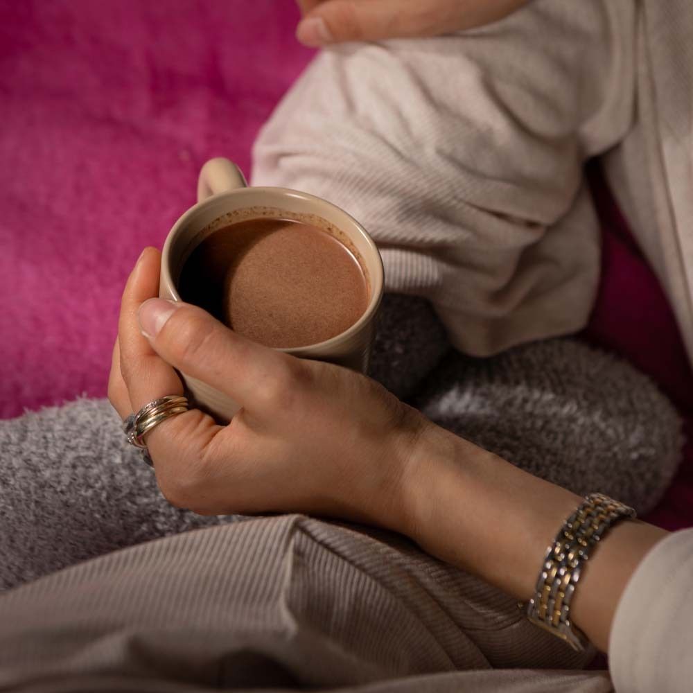Mains tenant une tasse de cacao. En arrière-plan, une couverture. Logo végan.