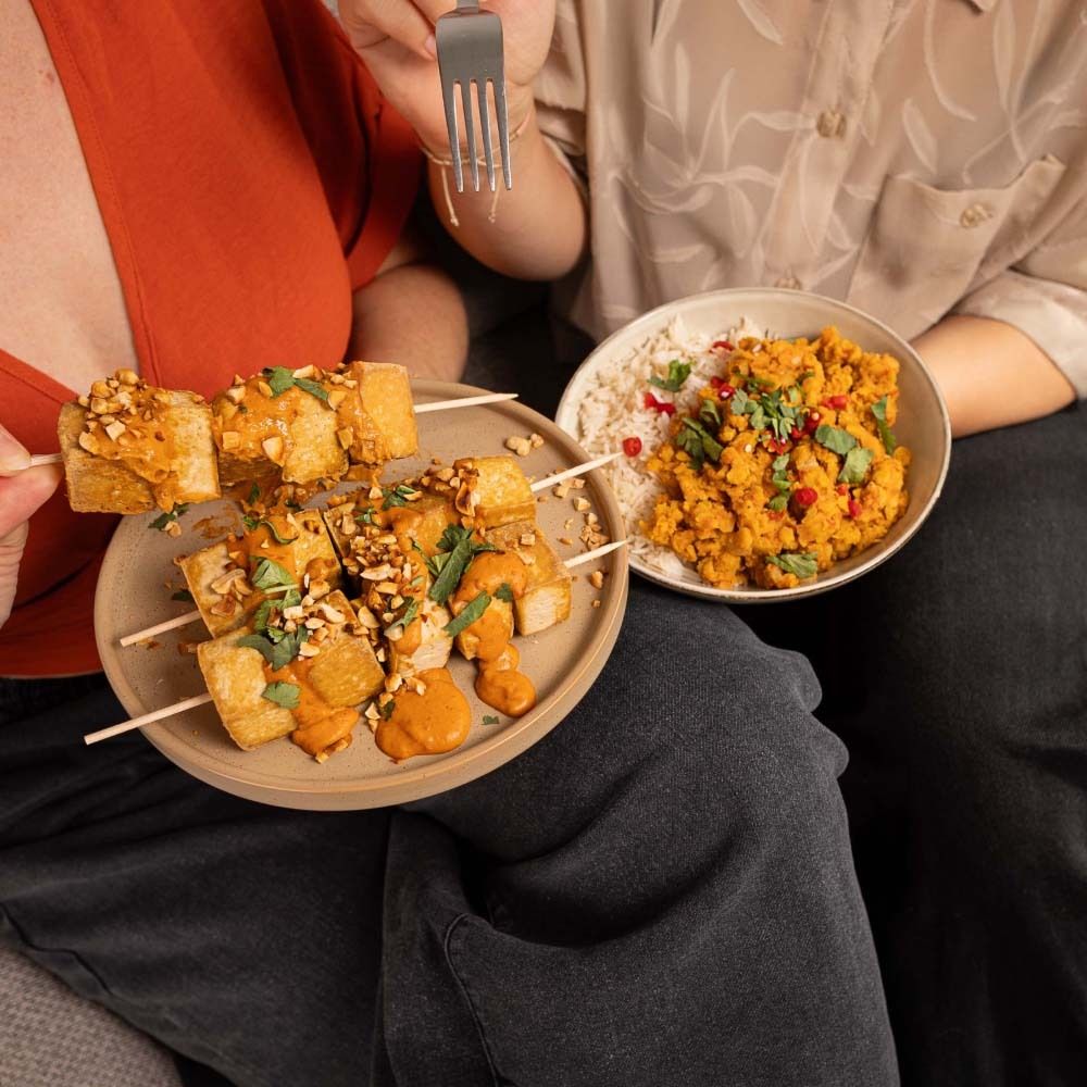 Mensen eten tofu-spiezen met pindasaus en linzencurry. Spiezen op een bord, curry in een kom.