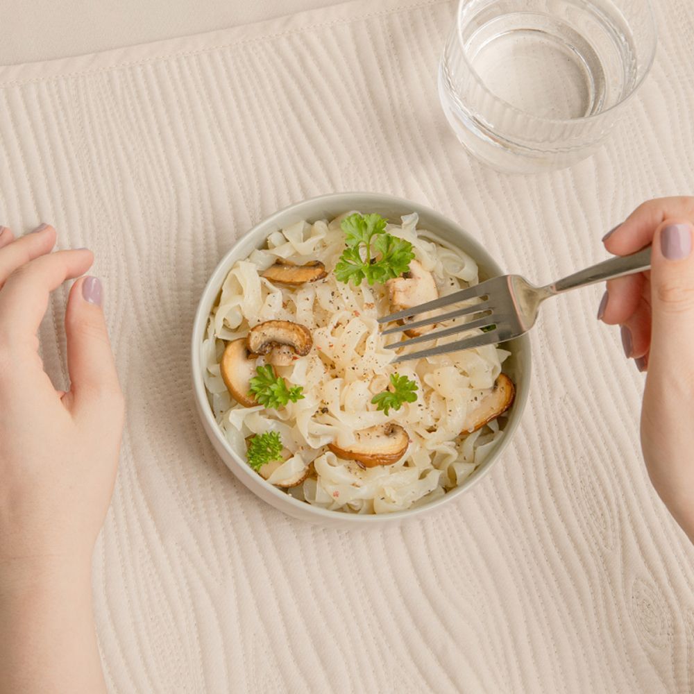 Un bol de Tagliatelle de konjac avec champignons et persil, tenu par des mains avec une fourchette.