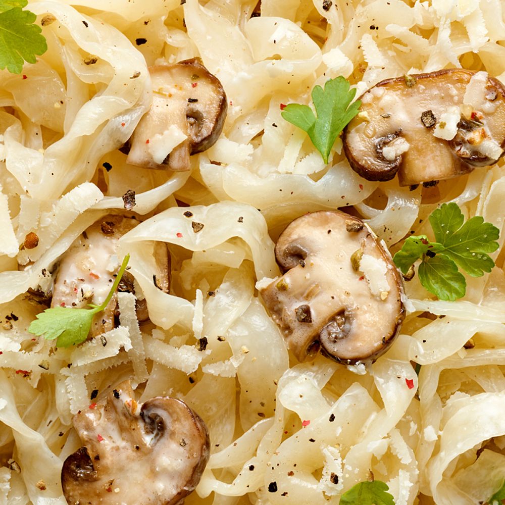 Gros plan de Tagliatelle de konjac avec champignons et persil, assaisonnée de poivre.