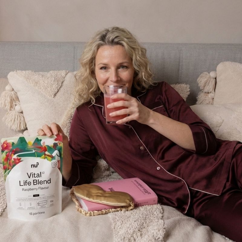 Femme buvant du nu3 Vital Life Blend au lit, sachet et masque de sommeil à côté.