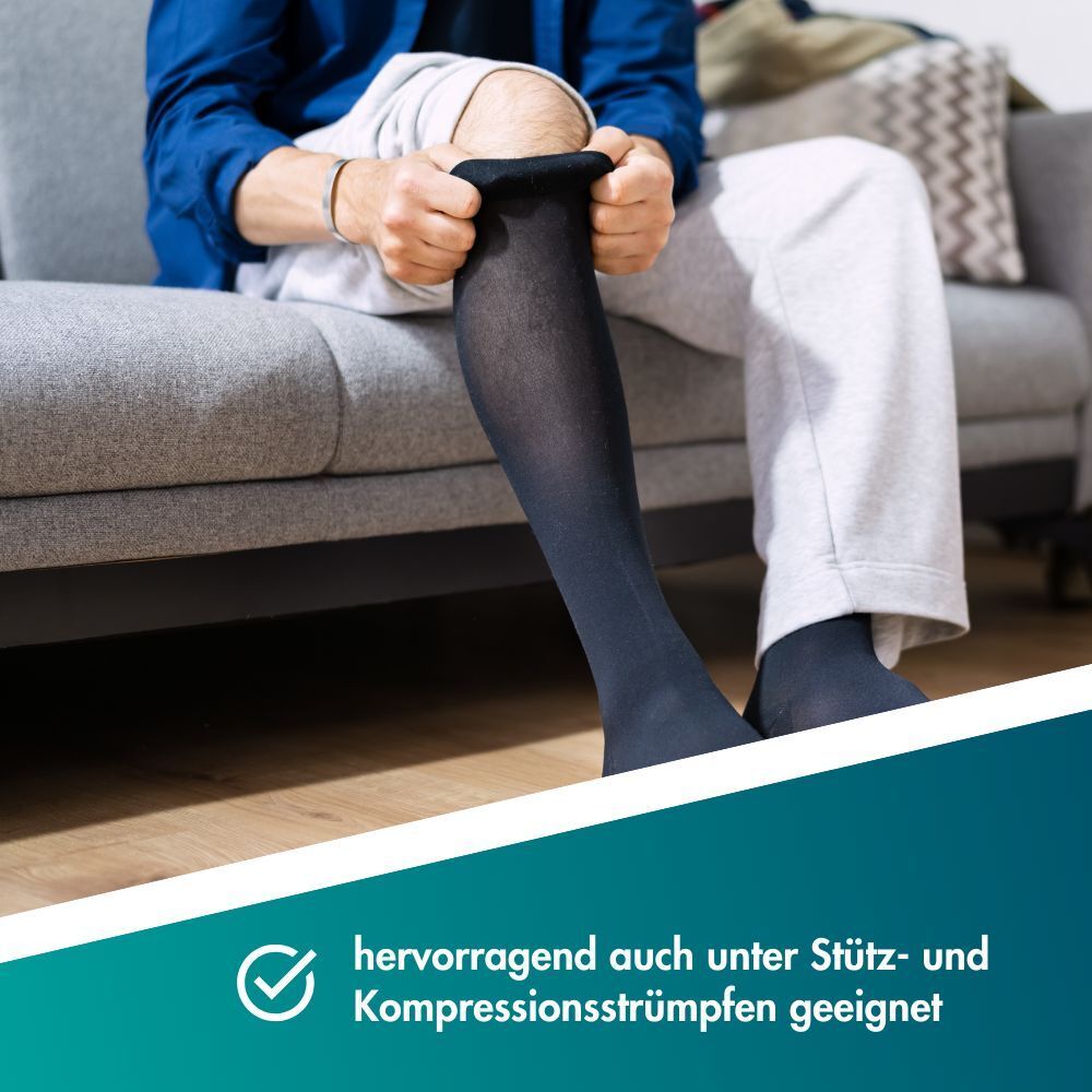 Personne enfilant des bas de compression, assise sur un canapé.