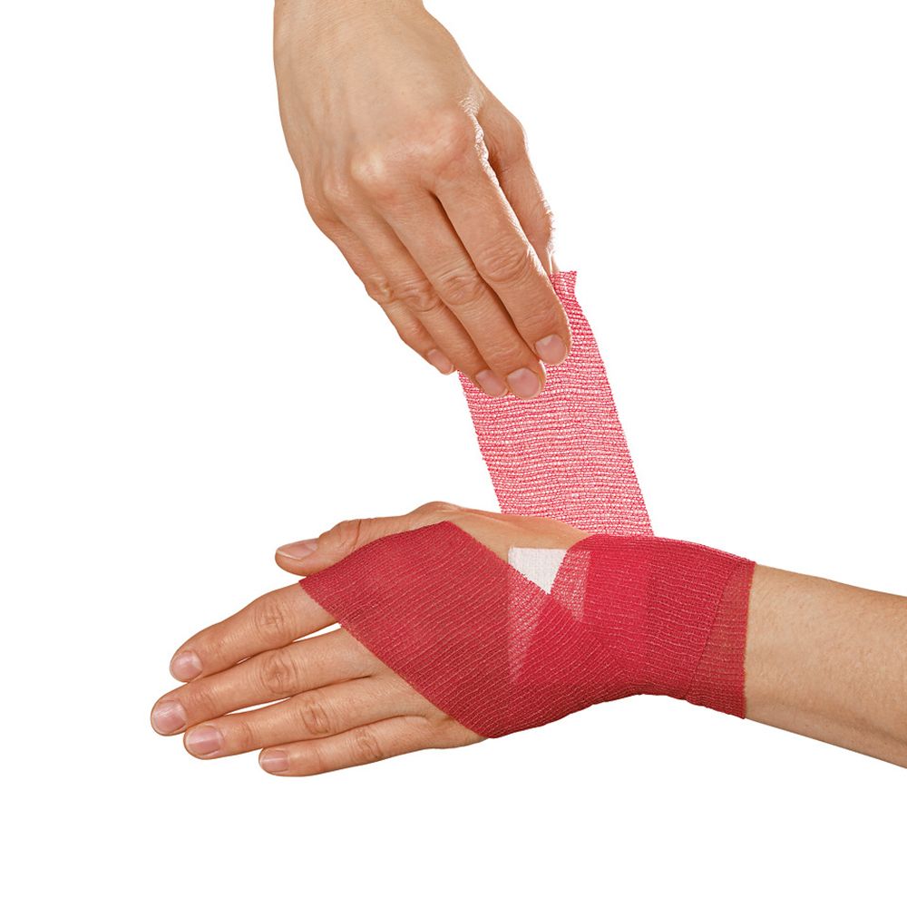 Rode fixatiewindsel wordt om een hand gewikkeld. Windsel is aangebracht. Handen in beeld.