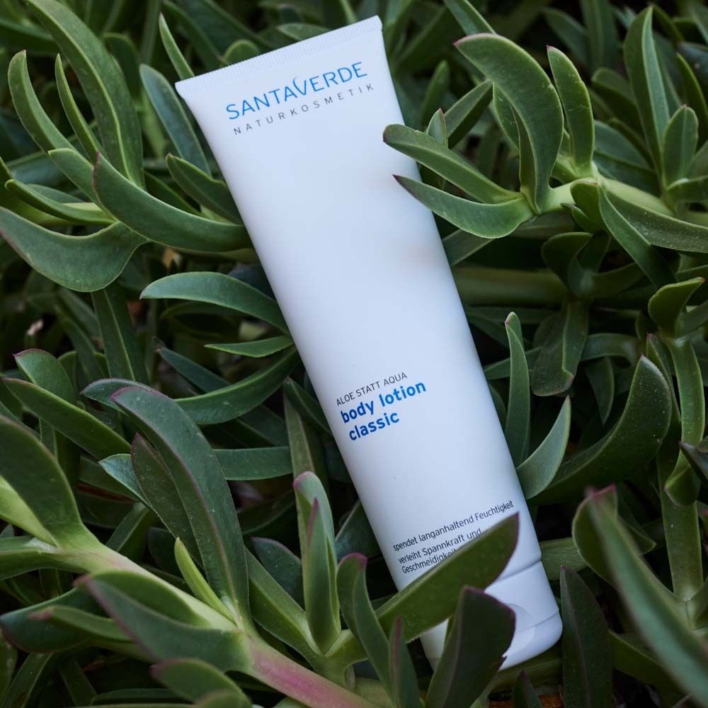 Witte tube met opschrift "SANTAVERDE NATURKOSMETIK" en "body lotion classic", omringd door groene vetplanten.
