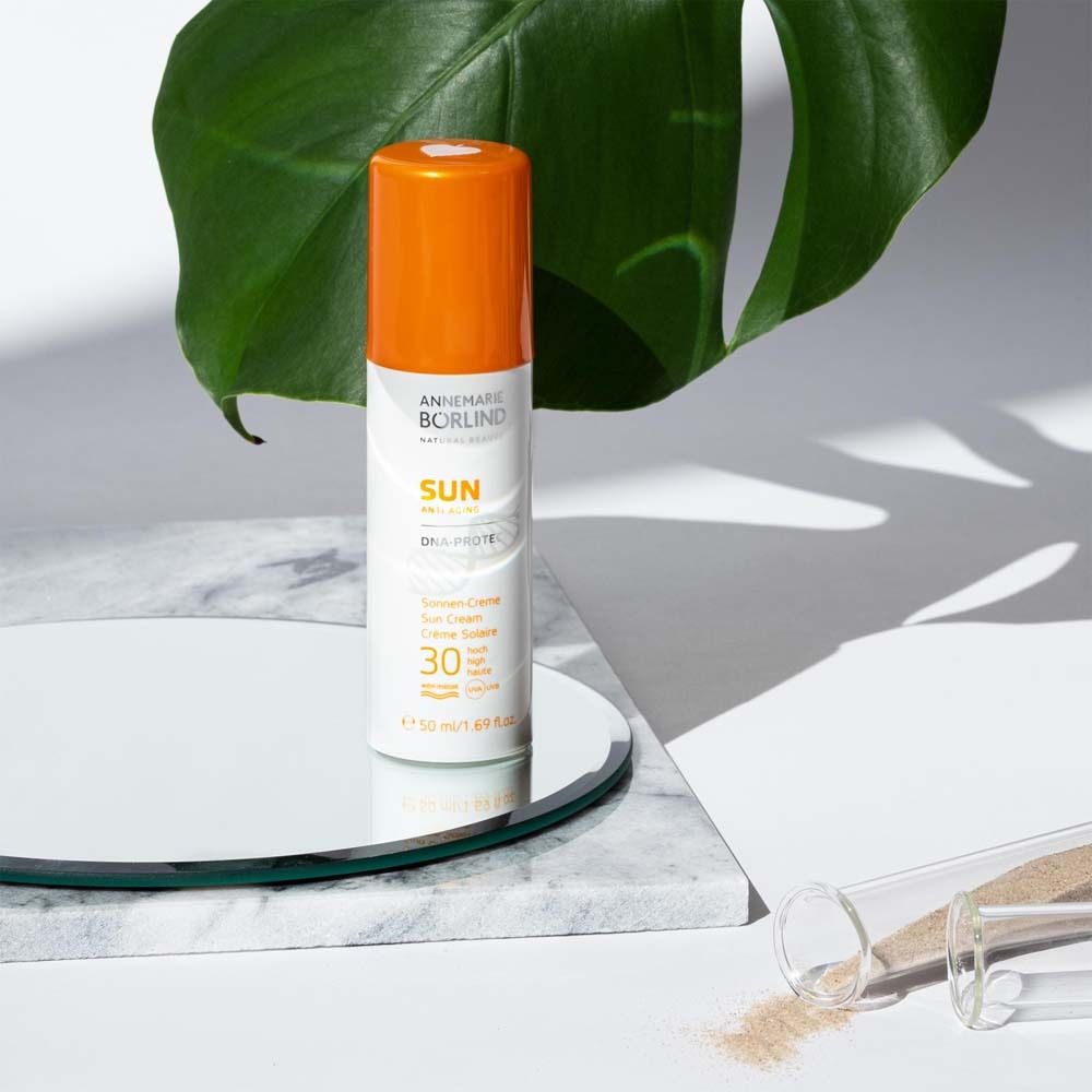 Tube de crème solaire avec bouchon orange sur miroir et feuille. Texte: ANNEMARIE BÖRLIND, SUN, SPF 30.