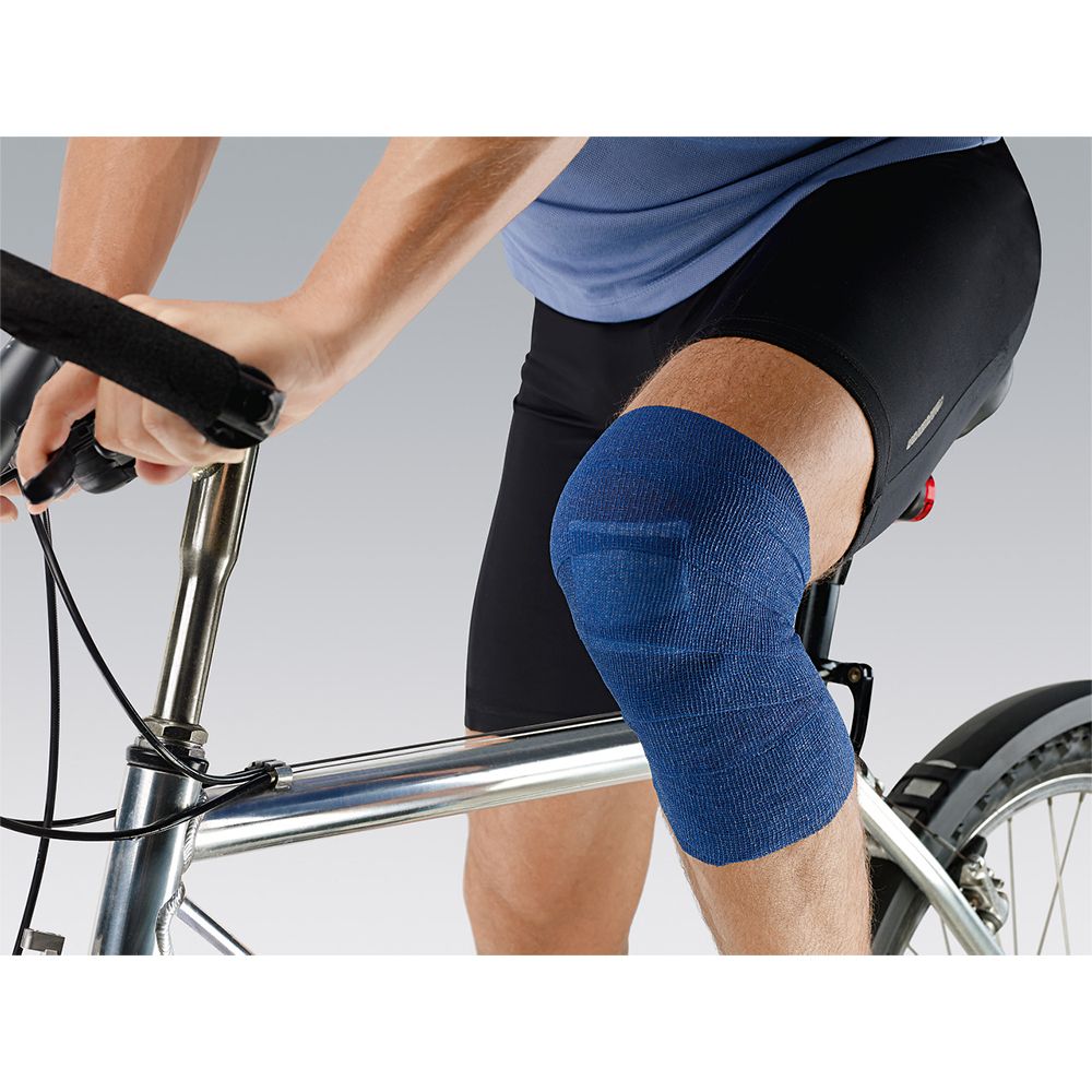 Persoon met blauw fixatieverband op de knie. Fietser op fiets. Verband bedekt het kniegewricht.