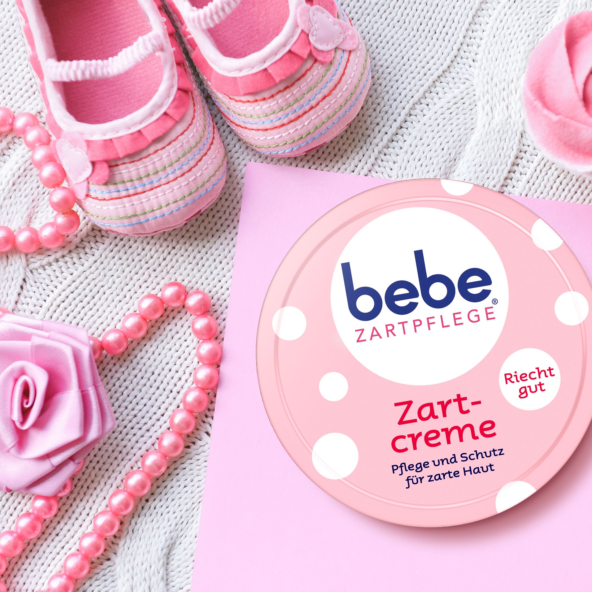 Roze pot bebe® Zartcreme, omringd door accessoires. Tekst: Zartcreme, Pflege und Schutz. Riecht gut.