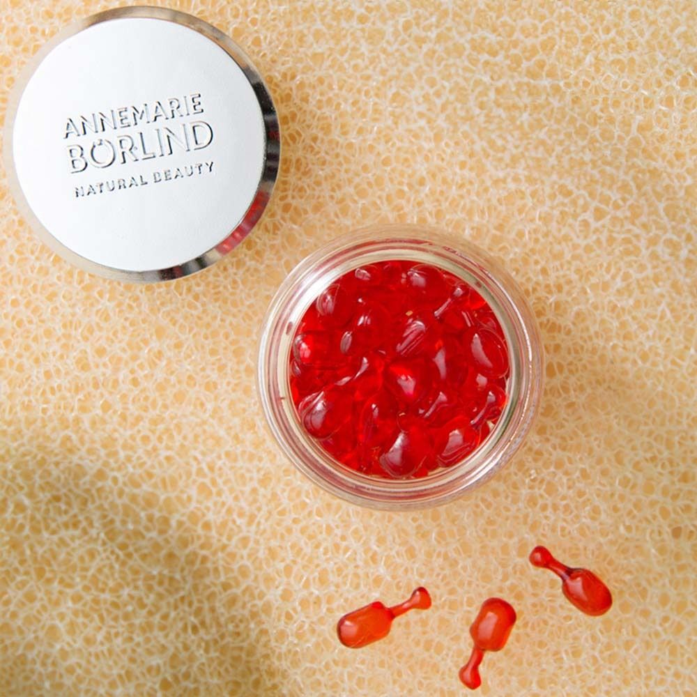 Glazen pot met rode capsules en deksel. Daarnaast drie losse capsules.