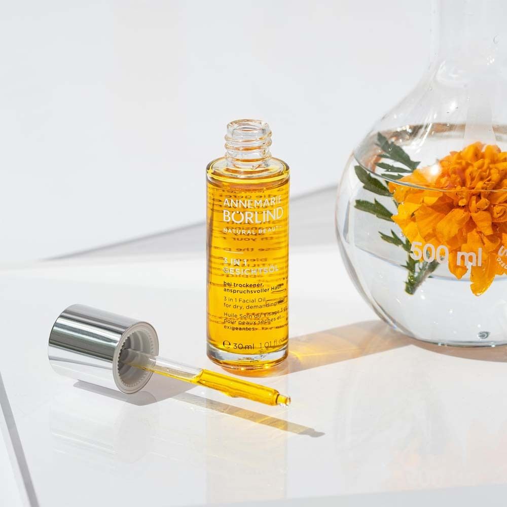 Gezichtsolie fles met pipet naast een bekerglas met bloem. Product: ANNEMARIE BÖRLIND, 3 in 1 Gezichtsolie.