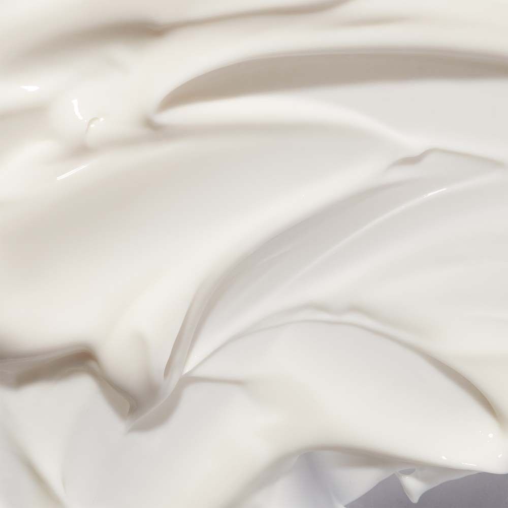 Gros plan sur une crème pour les mains blanche. Texture crémeuse, en forme de vagues. Pas d'étiquette visible.