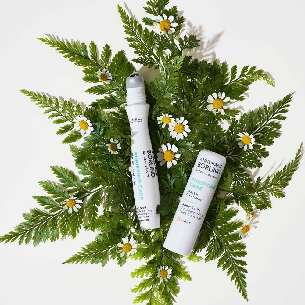 Twee roll-ons en een tube op bladeren en bloemen. Tekst: PURIFYING CARE. Merk: ANNEMARIE BÖRLIND.