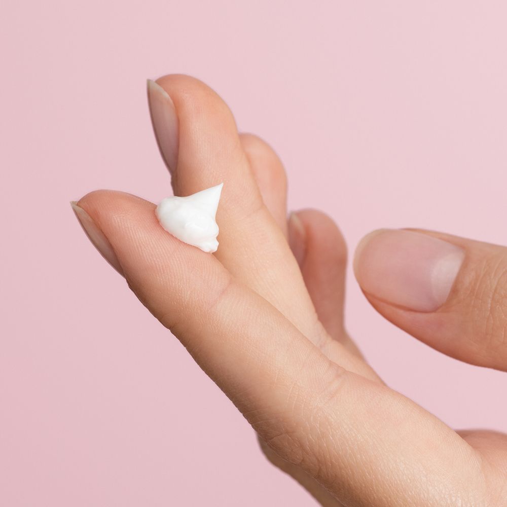 Kleine hoeveelheid witte crème op een vinger. Roze achtergrond.