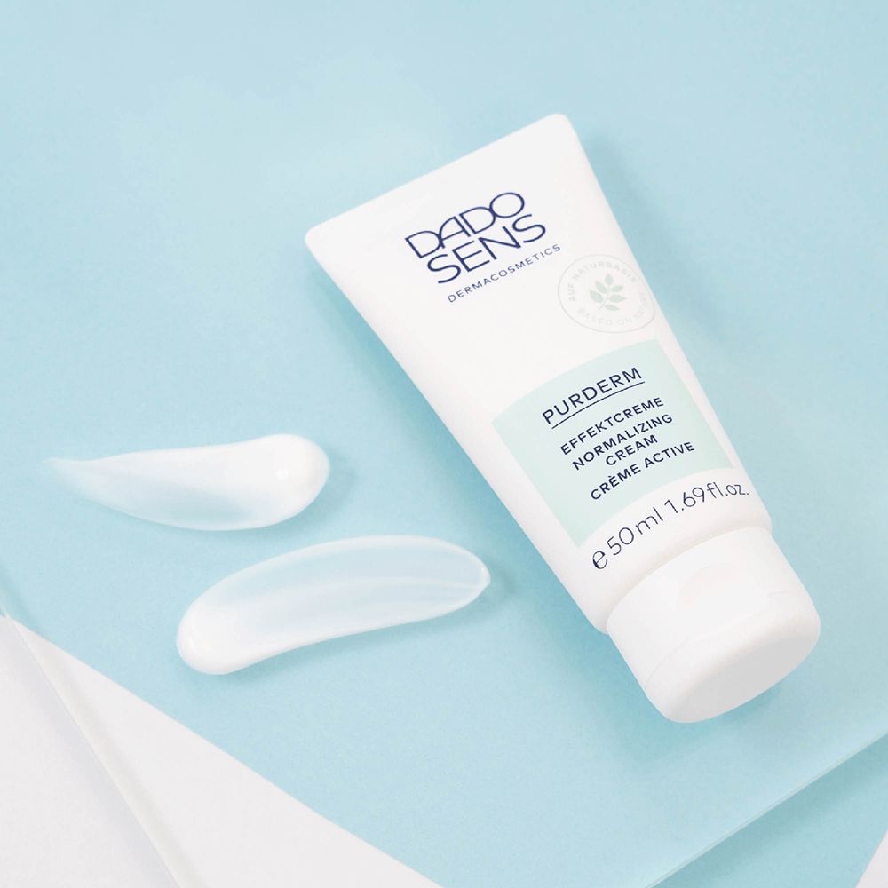 Witte crèmevlekken naast tube. Tube met DADO SENS-logo en productnaam. Lichtblauwe achtergrond.