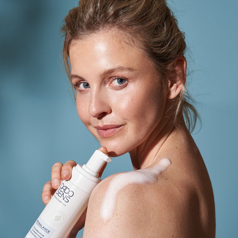 Femme avec mousse sur l'épaule. Flacon DADO SENS. Fond bleu.