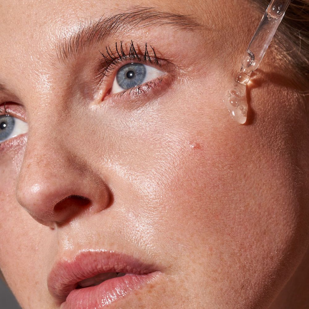 Gros plan sur une femme avec du sérum sur la peau. Une pipette dépose du sérum sur la joue.