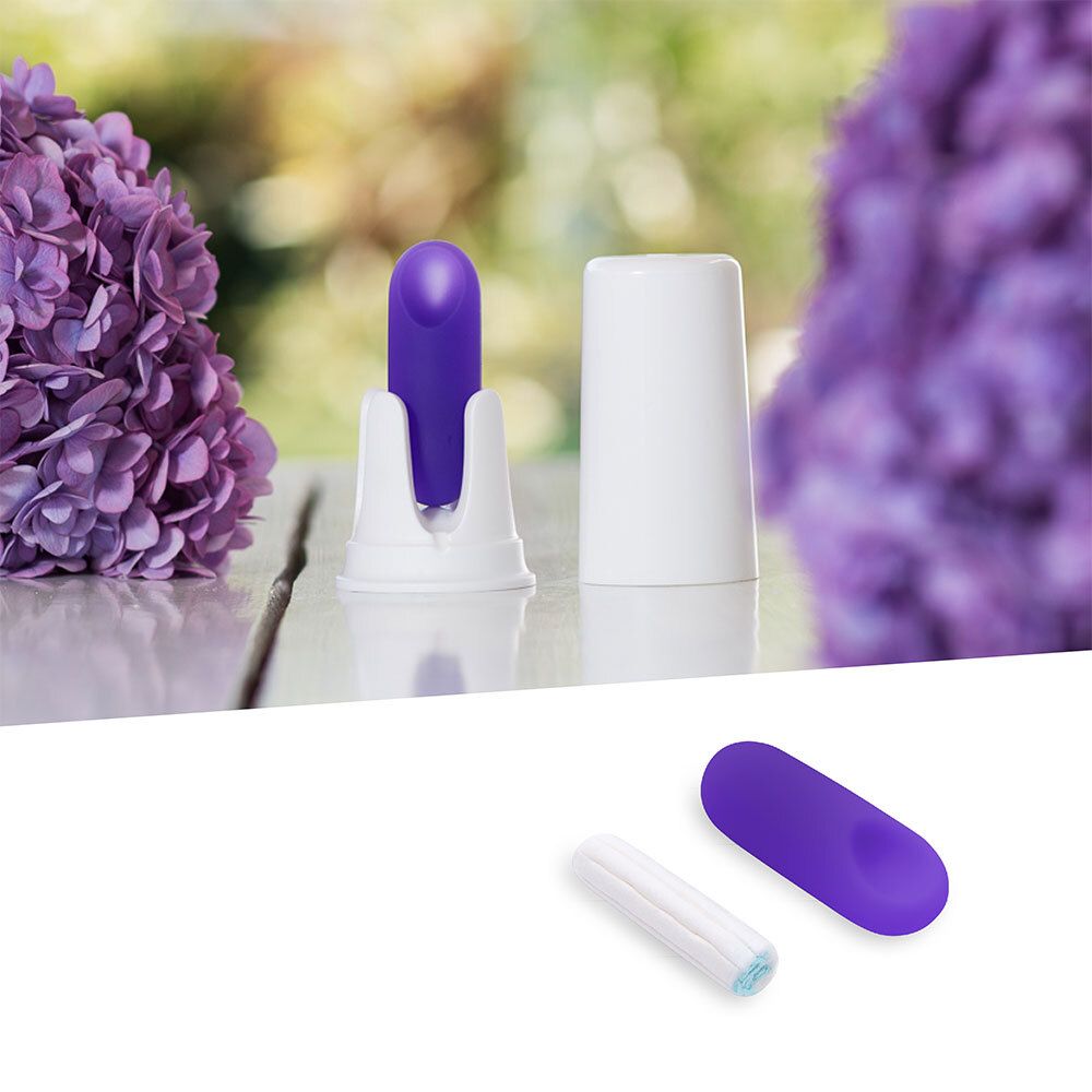 Paarse sensor in houder, witte container, daarnaast tampon en sensor. Achtergrond: bloemen.